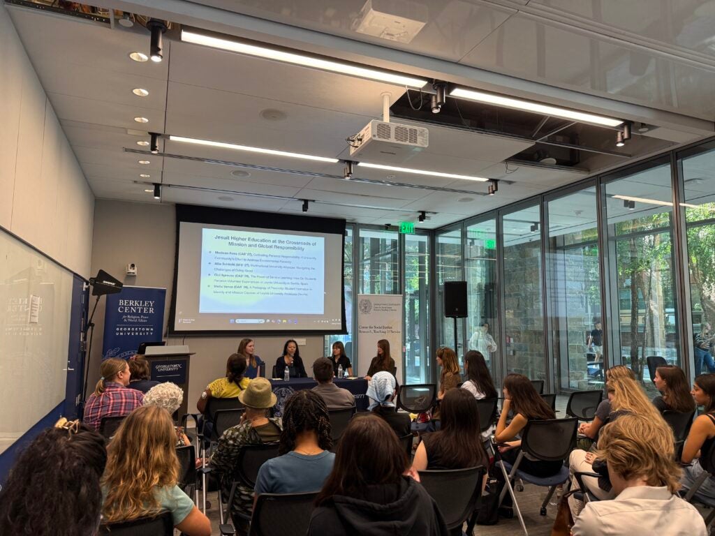 Photo from the back of the audience showing the symposium with a panel of four students.