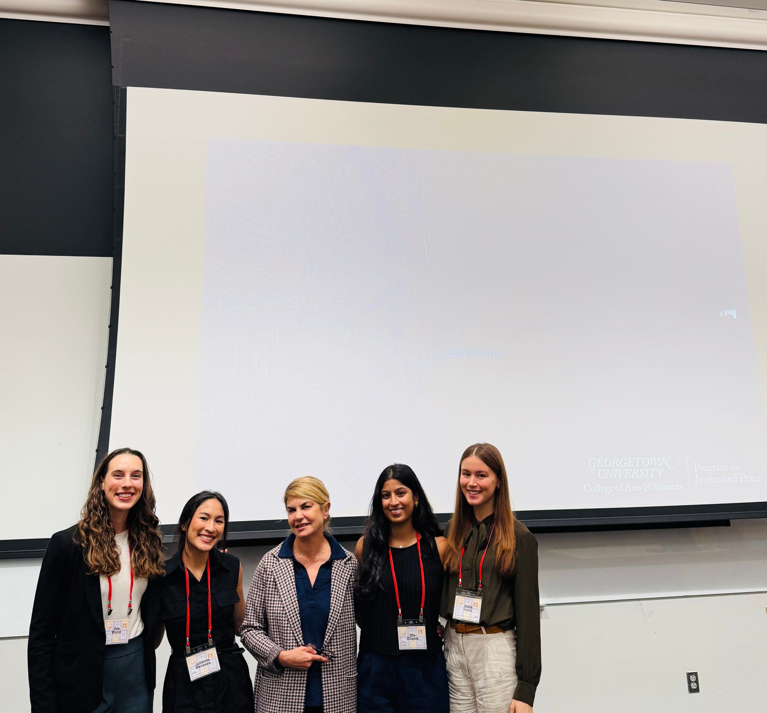 Four students and Professor Elham Atashi standing in professional clothing in front of a presentation screen.