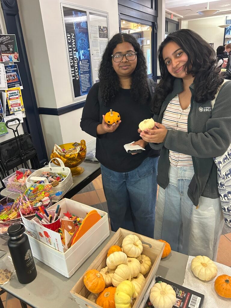 Two students pictured holding pumpkins in front of a table with Halloween candy and decorations.