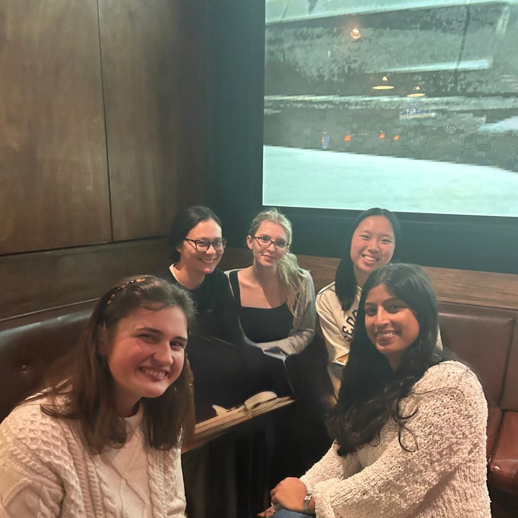 5 JUPS seniors sit gathered around a table and smiling.