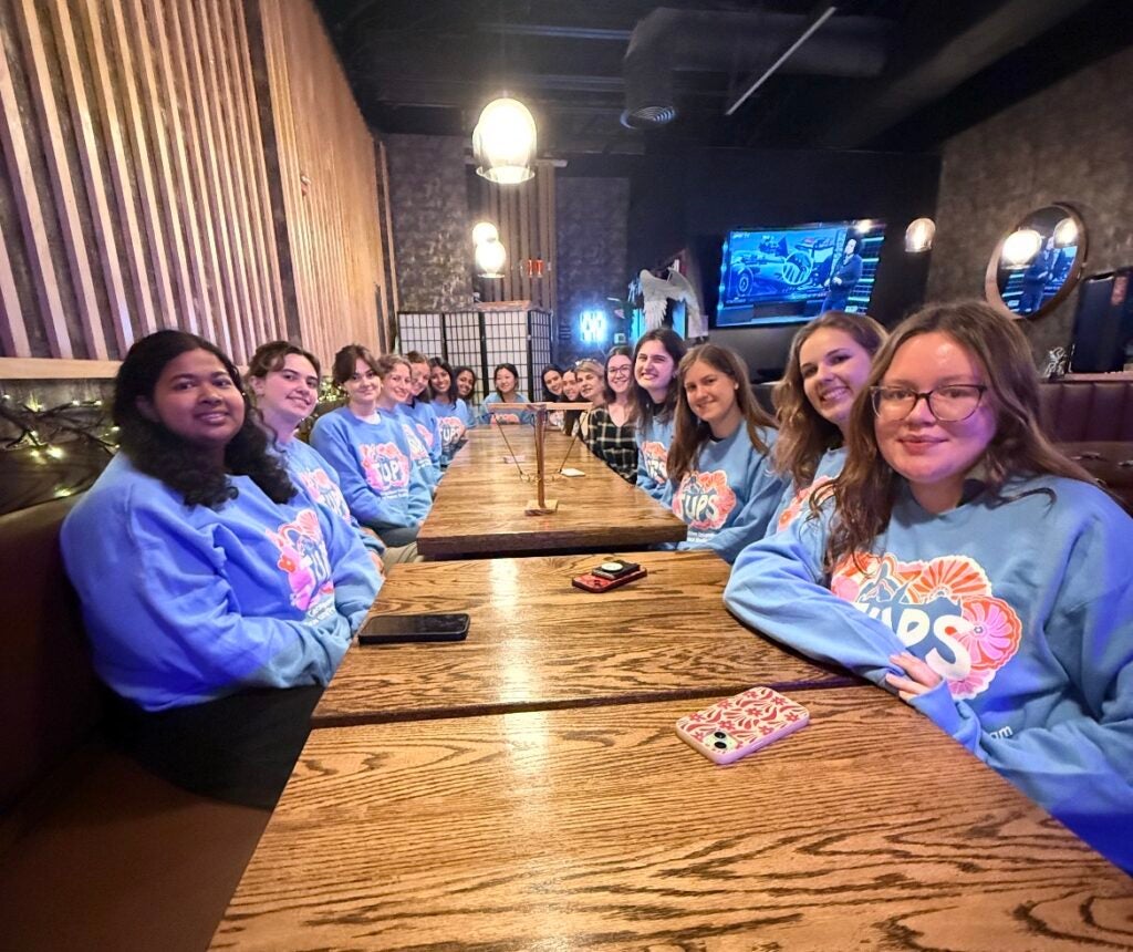 A table of 20-25 students sit at Tai Chi restaurant, all wearing blue sweatshirts with the JUPS logo.