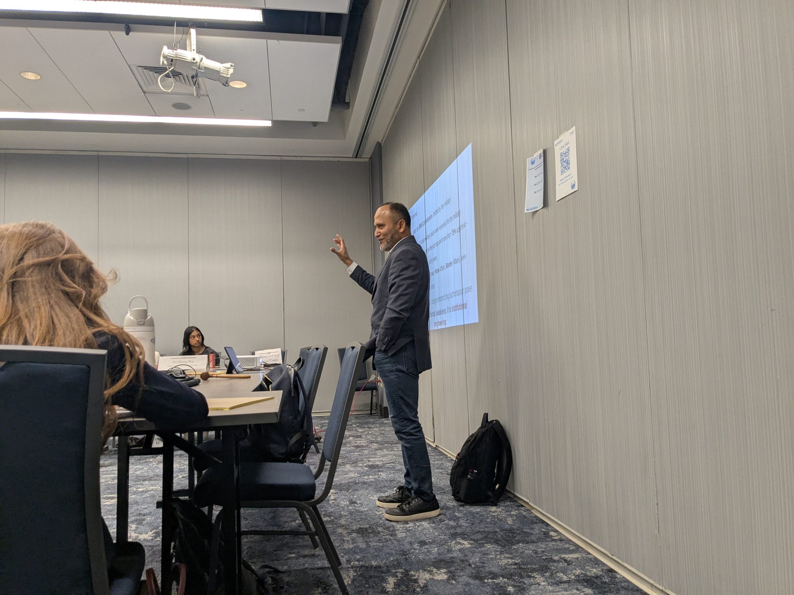 Photo of Professor Khan presenting in front of a slideshow.